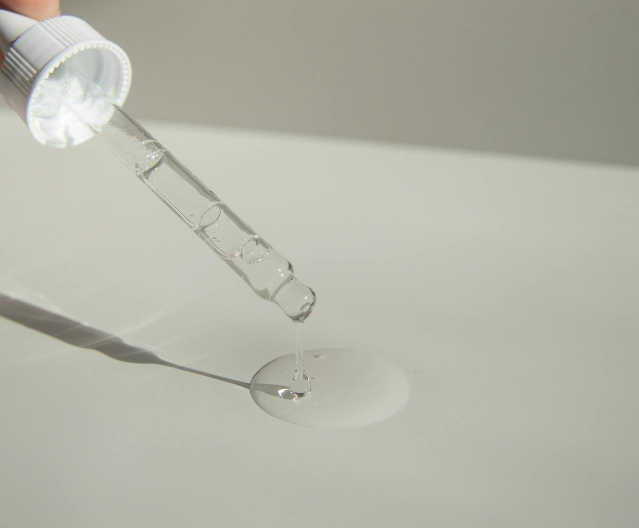 about-01 Close-up of a cosmetic pipette releasing serum onto a surface with soft sunlight.